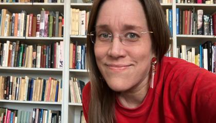 Henkilö istuu kirjastosalissa ja katsoo kameraan.