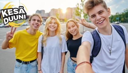 Neljä nuorta hymyilee kameralle auringon paisteessa. He ovat pukeutuneet kesäisiin värikkäisiin vaatteisiin.