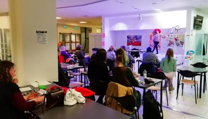 Pikapiirustustyöpaja kahvilamiljöössä. Etualalla opiskelijoita. Taustalla on elävä malli.