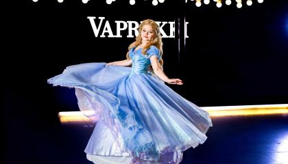 Vaaleahiuksinen tyttö sinisessä leveähelmaisessa mekossa pyörähtämässä Vapriikin aulassa.