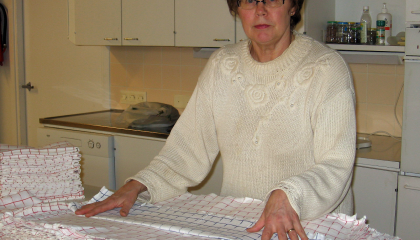 Henkilö seisoo opetuskeittiössä. Taustalla on tiskiallas, ja pöydällä on viikattuja liinoja.