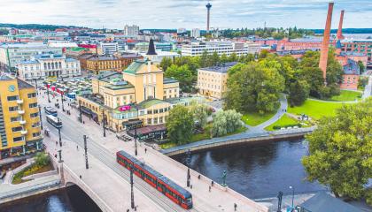 Punainen ratikka ajaa Hämeensiltaa pitkin kohti Tampereen Keskustoria kesäisenä päivänä ja taustalla horisontissa näkyy Näsinneula.