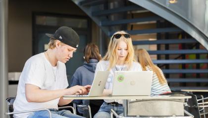 Kaksi opiskelijaa istuu pöydän ääressä ja työskentelee tietokoneilla.