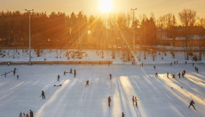Luistelijoita Sorsapuiston tekojäällä, aurinko paistaa matalalta.