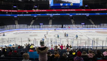 Jääkiekkoa pelaavat lapset kentällä, etualalla lapsiyleisöä selin.