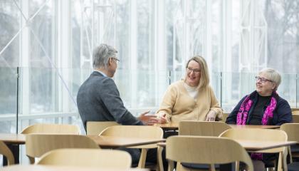 Kolme henkilöä istuu keskustelemassa pöydän ääressä.