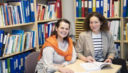 Kaksi henkilöä istuu pöydän ääressä täysinäisen kirjahyllyn edessä.