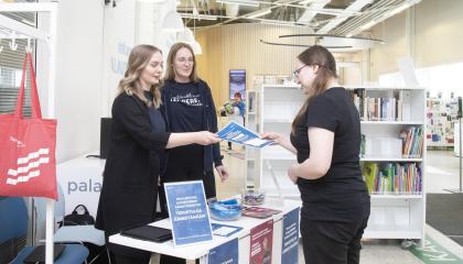Kaksi kaupungin työntekijää keskustelemassa asukkaan kanssa. Toinen työntekijöistä ojentaa esitettä asukkaalle.