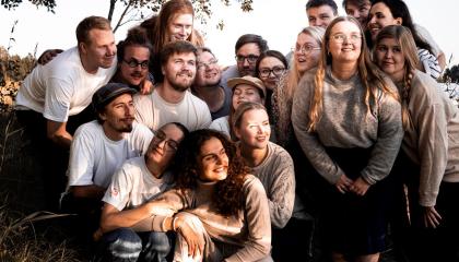 Ryhmä nuoria aikuisia hymyilee ja katselee kohti taivaanrantaa.