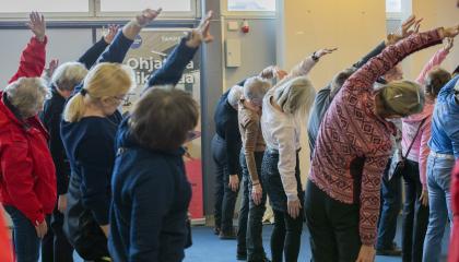 Senioreita osallistumassa liikuntatuokioon ja jumppaamassa seisten.