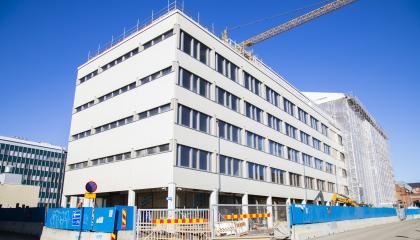 Valkoinen virastotalon etualalla ei näy enää rakentamisen aikaista suojahuppua, mutta osassa taloa se vielä on. Talon ympärillä on rakentamisen aikainen aita.