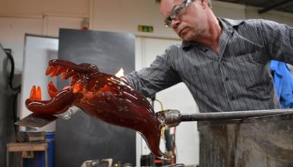 Lasinpuhaltaja Johannes Rantasalo työstämässä terävähampaista, punertavaa lasihirviötä.