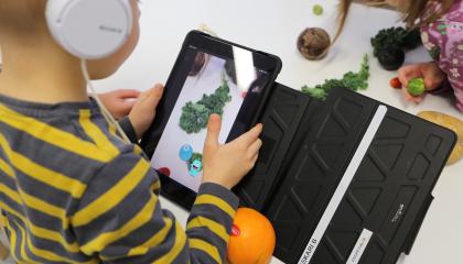 Esikouluikäinen lapsi kuvaa kasviksia tabletin kameralla ja tunnistaa niitä Vegemi-sovelluksen avulla.