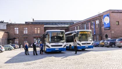 Kaksi sinivalkoista bussia rakennuksen pihalla. 