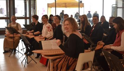 Henkilö soittaa kannelta. Hänen takanaan on ryhmä muita soittajia.