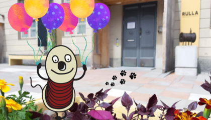 Piirretty Rulla-hahmo pitää tassuissaan keltaisia, violetteja ja vaaleanpunaisia ilmapalloja. Taustalla Rullan sisäänkäynti.