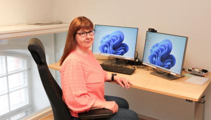 Henkilö istuu työpöydän ääressä ja katsoo kameraan.