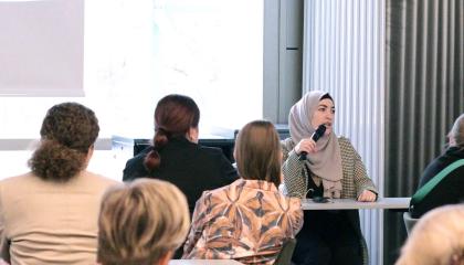 Henkilö puhuu monimuotoiselle yleisölle kokoustilassa. 