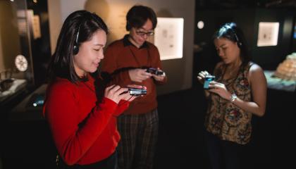 Kolme henkilöä kuuntelee ääniopastusta Muumimuseossa.