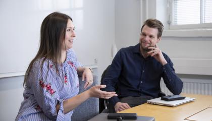 Hankintapalveluiden työntekijät Heini Kuoppamäki ja Jarkko Vesapuisto istuvat pöydän ääressä ja juttelevat.
