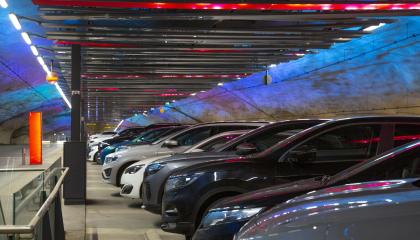 Henkilöautoja rivissä parkkihallissa, jonka harmaille tunneliseinämille heijastuu sinisen eri sävyjä.