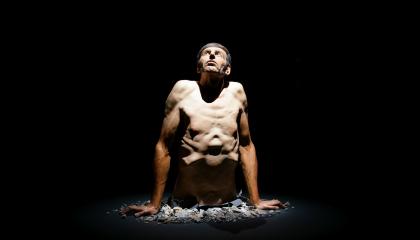 Valokuva hyperrealistisesta veistoksesta, jossa miehen ylävartalo nousee lattiasta. 