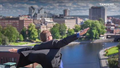 Henkilö levittää kätensä kuin lentokoneen siiviksi. Taustalla Tampereen kaupunkinäkymä. 