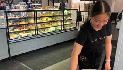 Nuori naishenkilö pyyhkii pöytää kahvilassa.