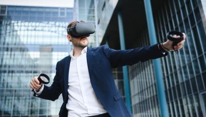 Mies seisoo modernin lasirakennuksen edessä vr-lasit päässään ja sensorit käsissään.