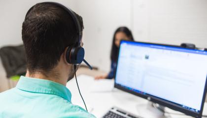 Henkilö katsoo tietokonetta kuulokkeet päässä.