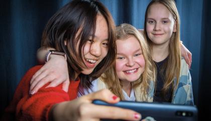 Kolme nuorta ottamassa selfietä sinistä taustaa vasten.
