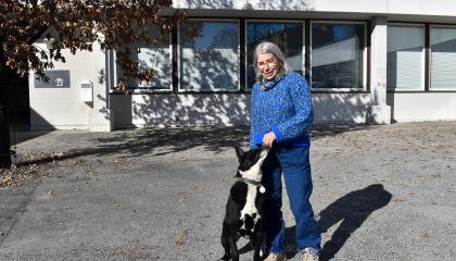 Henkilö seisoo koulun edessä koiransa kanssa. Koira nuuhkii omistajan käsiä.