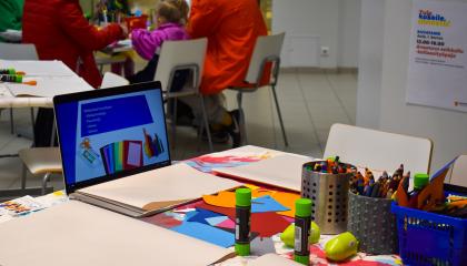 Askartelutarvikkeita pöydällä. Vieressä on tietokone, jonka näytöllä on ohjeita.