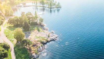 Aurinkoinen järvenrantamaisema ylhäältä päin kuvattuna.