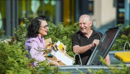 Nainen laittaa pahvijätettä kartonginkeräysastiaan miehen pitäessä kantta auli.