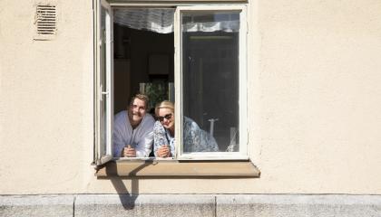 Mies ja nainen kurkistavat vaalean rakennuksen ikkunasta.