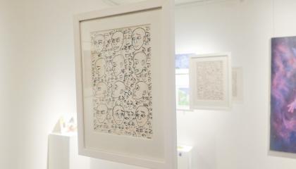 Yleiskuva galleriasta, jossa etualalla näkyy teos, jossa on piirrettynä erilaisia ilmeitä.