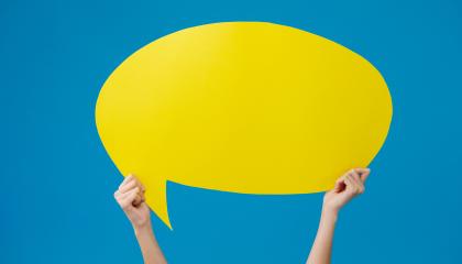 Kädet pitelevät kirkkaan keltaista puhekuplaa.