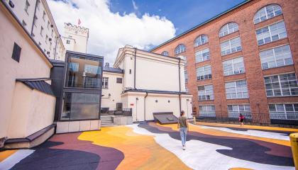 Värikäs katumaalaus Finlaysonin tiilirakennusten välissä, yksittäisiä ihmisiä kulkee alueella.