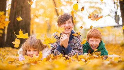 Kolme hymyilevää lasta syksyisten lehtien keskellä.