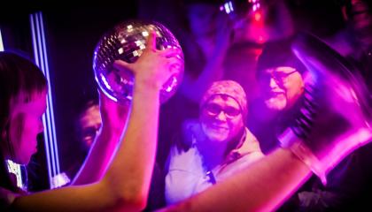 Diskopalloa käsissään pitävä hahmo esiintyy ikkunan takana kadulla seisovalle yleisölle. 