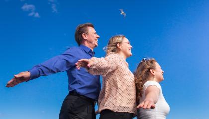 Kolme henkilöä kuvattuna taivasta vasten. He kaikki katsovat samaan suuntaan ja heidän kätensä ovat levällään ikään kuin he olisivat lähdössä lentoon.