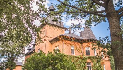 Suuri punatiilinen kartanorakennus pilkistää puiden lomasta.