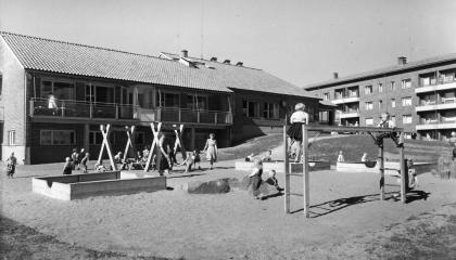 Mustavalkoisessa kuvassa Kalevan lastentalon pihamaan leikkialuetta, jossa muun muassa hiekkalaatikko ja kiipeilyteline.