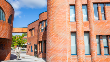 Reima ja Raili Pietilän suunnittelemia punatiilisiä rakennuksia Hervannan keskustassa. Talojen välissä kävelee hervantalainen.