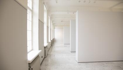 Isossa galleriatilassa on toisella seinällä ikkunoita ja kolme valkoista seinäkettä.