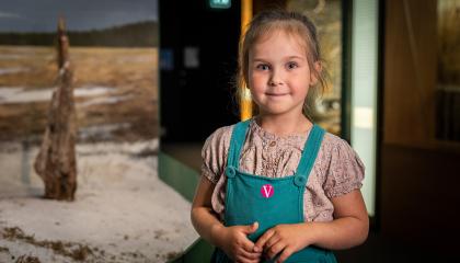 Pieni tyttö hymyilee kameralle, taustalla museon näyttelyä.