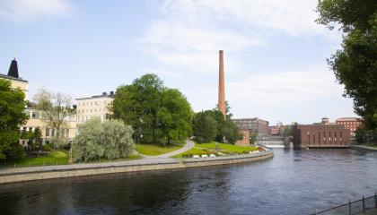 A river. On the backround pale yellow buildings on the left, a chimney in the center and red brick buildings on the right.