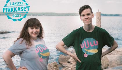Kaksi henkilöä hymyilee kameralle järven rannalla. Ylhäällä vasemmalla teksti: Lasten Pirkkaset 2025.