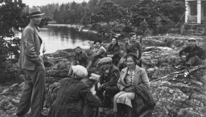 Henkilöitä istuu kalliolla. Taustalla on järvimaisema.